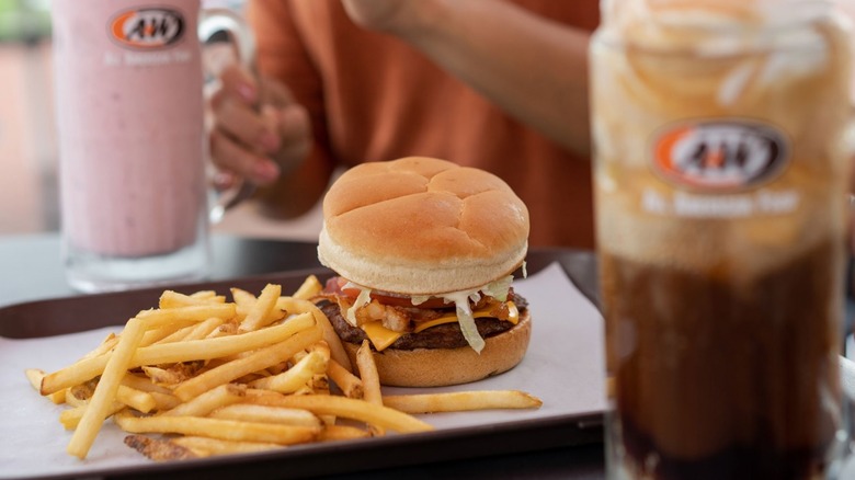 A&W fries are on a tray next to a burger with drinks in mugs on the side.