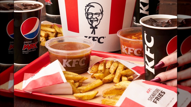 KFC fries spill out on a tray with sauce and a drink.