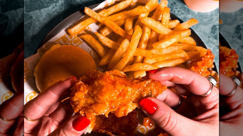 A Golden Chick hot wing is being held up with fries behind it on the table.