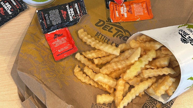 Del Taco crinkle-cut fries and sauce packets are displayed on a table.