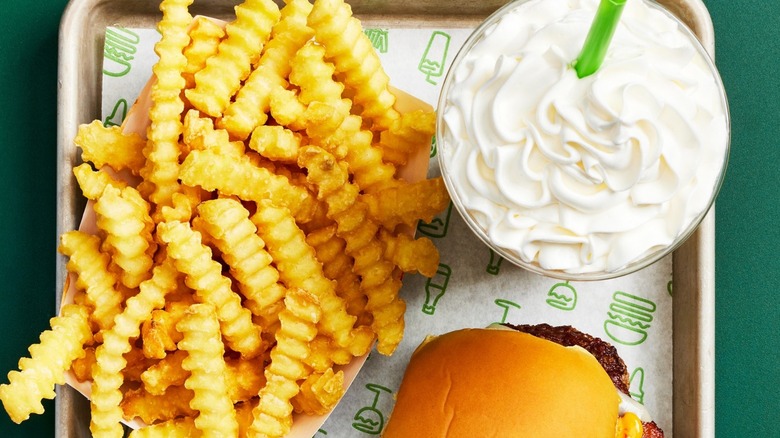 Shake Shack fries and a shake are on a tray next to a burger.