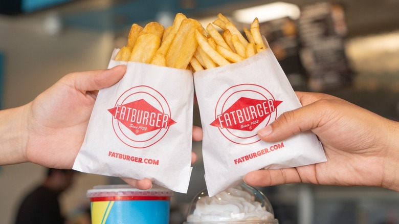 Hands are holding two orders of Fatburger french fries.