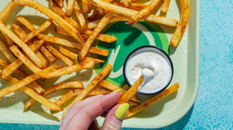 Wahlburgers fries are spread out on a tray with dipping sauce.