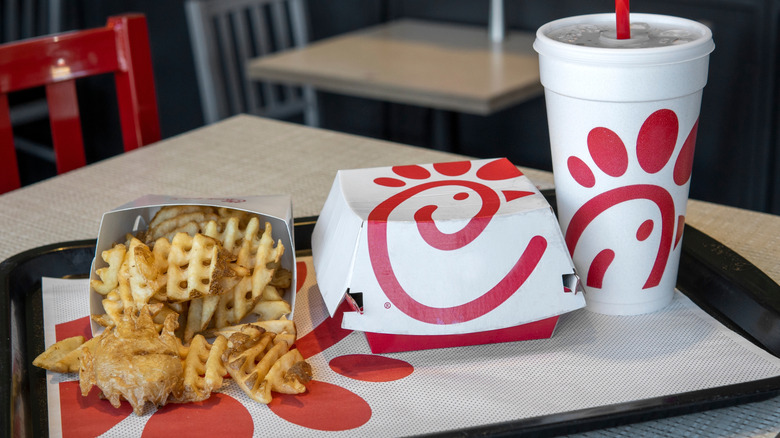 Chick-fil-A waffle fries sit on a tray in a restaurant with a sandwich box and a drink.