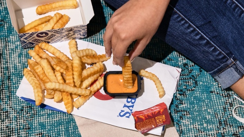 A pile of Zaxby's fries are spread on a napkin with someone dipping a fry in sauce.