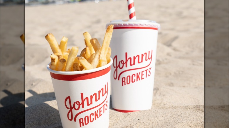 Johnny Rockets fries and a drink are sitting in the sand on the beach.