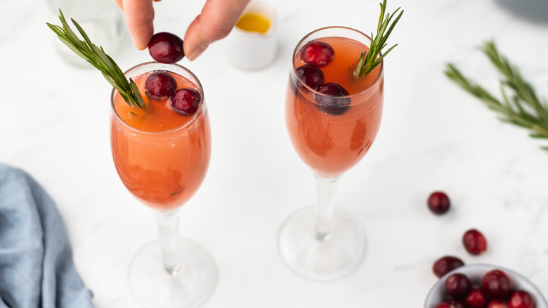 Two cranberry mimosa cocktails garnished with cranberries and rosemary