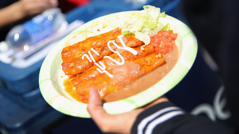 Hand holding plate of enchiladas with beans and lettuce