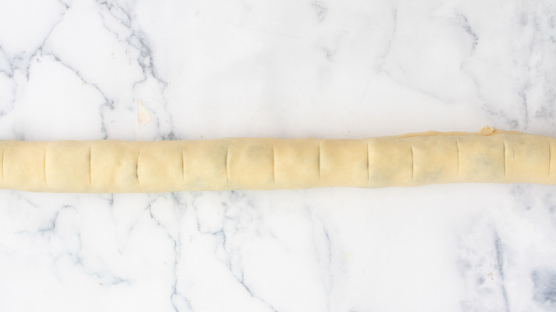 long roll of dough with indentations on a white countertop