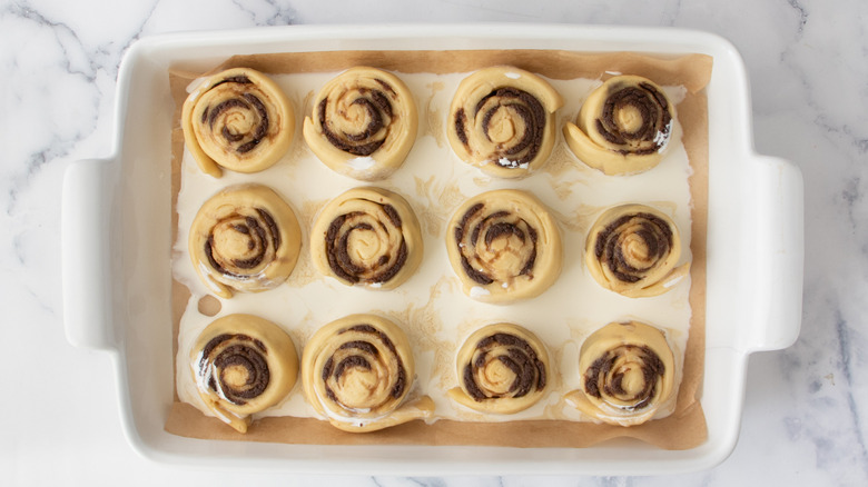 dough pinwheels in white liquid in a white pan on a white countertop