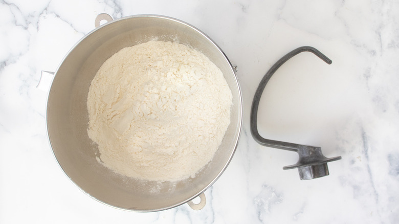 flour in a metal bowl on a white countertop next to a metal hook