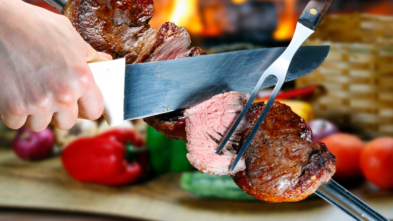 Knife and fork removing picanha from spit 