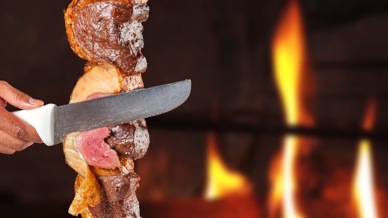 A knife slicing picanha on a spit 