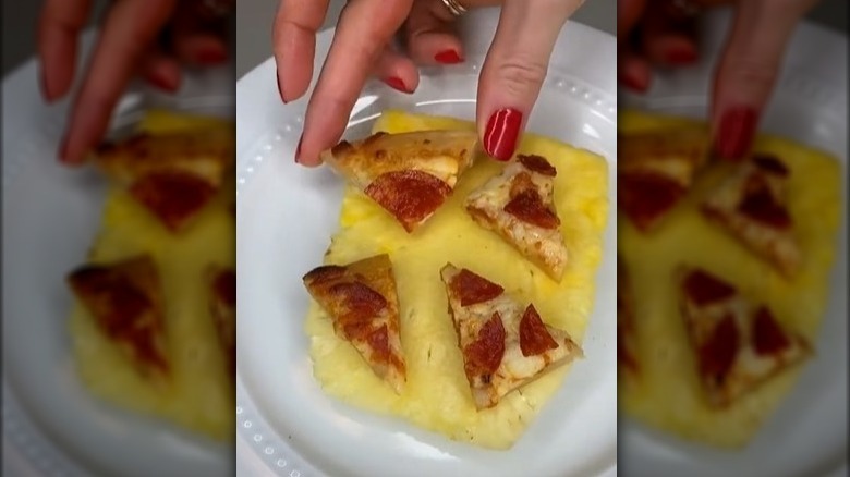 A person putting small pieces of pepperoni pizza on a slice of pineapple.