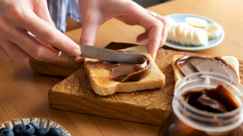 hand spreading peanut butter on toast with knife