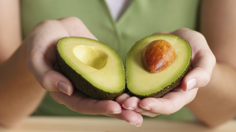 Hands holding two halves of an avocado