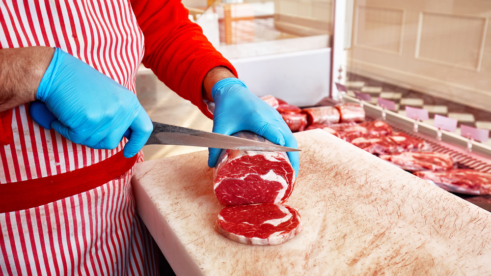 Butcher cutting meat on white cutting board