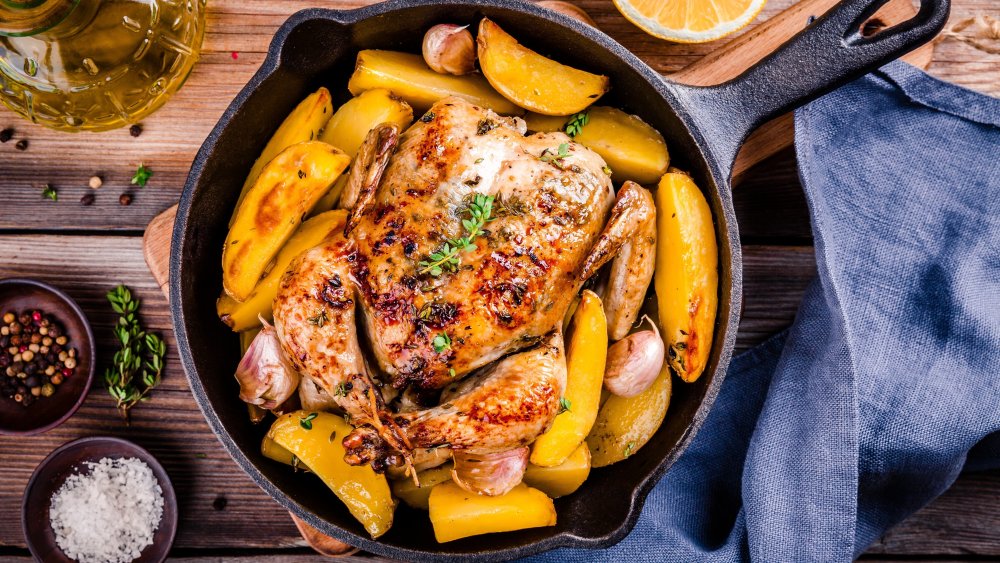 Whole roast chicken with potatoes and thyme in cast iron