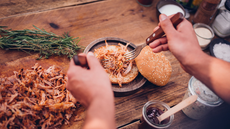 Person putting shredded meat on a bun