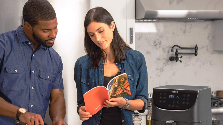 A man and woman preparing a meal using the Cosori Air Fryer and cookbook