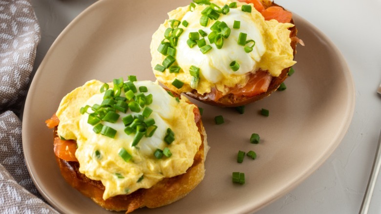 Eggs benedict topped with chives on a white plate