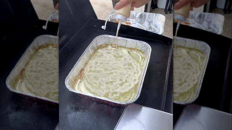 Person making funnel cakes on flattop grill with aluminum baking dish full of frying oil