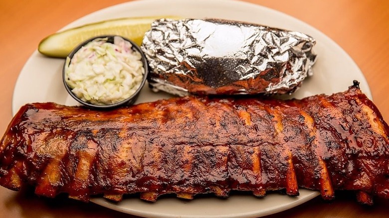 Barbecue ribs, coleslaw, pickles, and foil-wrapped potato