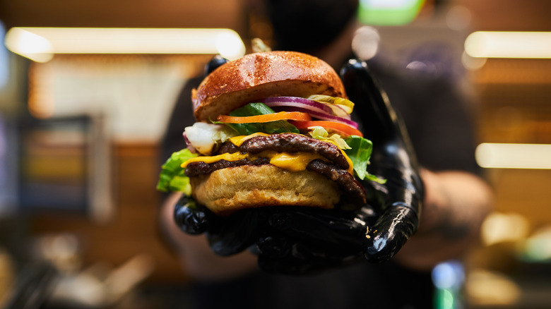 Person with black gloves holding a burger