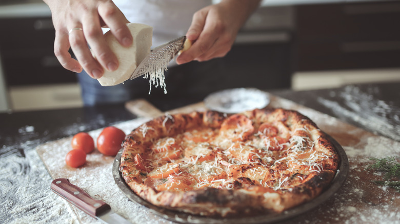 Person grating mozzarella onto pizza