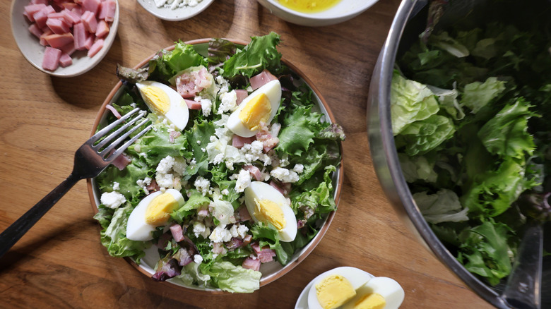 plated bistro salad surrounded by bowl of greens and dishes of toppings