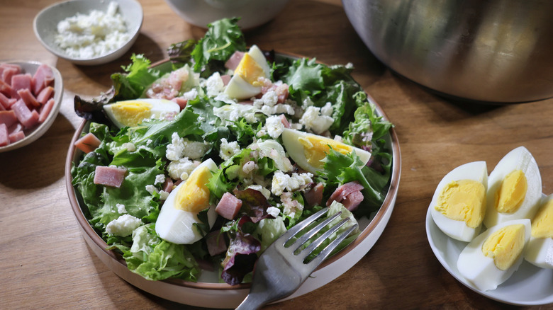 French bristro salad on a plate topped with boiled eggs, ham, and chevre