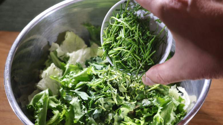 hand pouring chopped chives to bowl of mixed lettuces