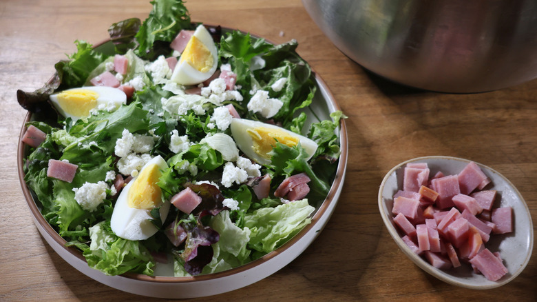 plated salad topped with boiled eggs, ham, and chevre