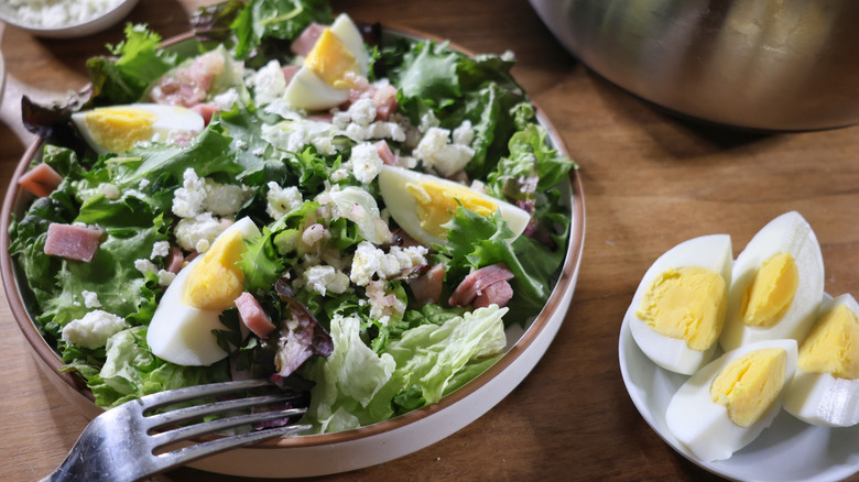 plated salad with boiled eggs, ham, and chevre, with small dish of chopped eggs alongside