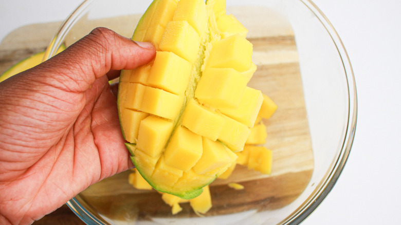 A hand holding cut-up mango