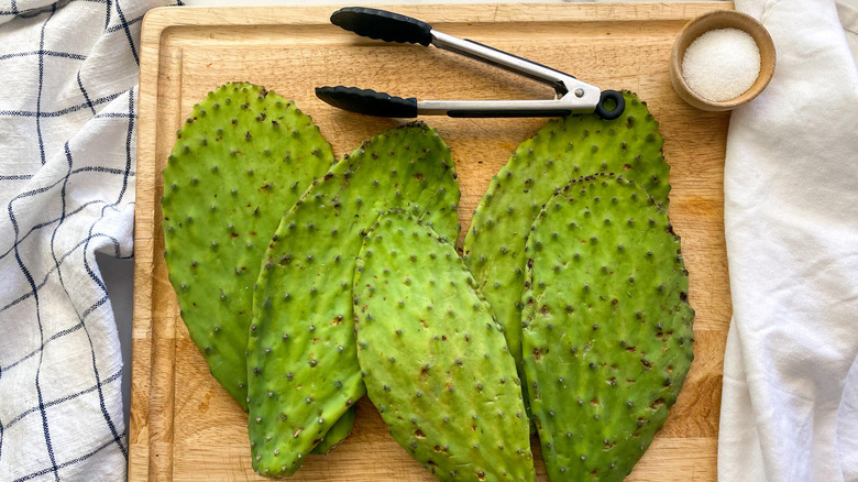 Fresh prickly pear cactus nopales on wooden cutting board with tongs