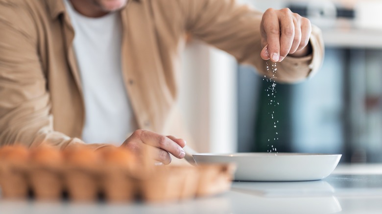 man sprinkling salt on eggs