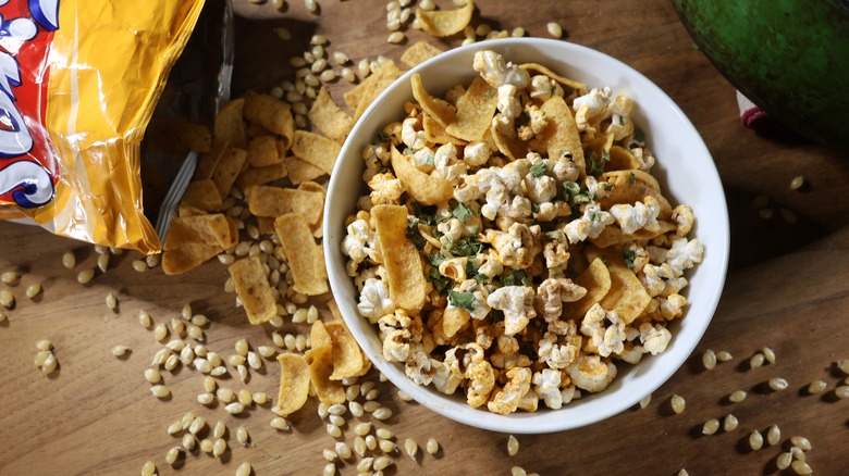 bowl of Frito pie popcorn on wooden table with spilled Fritos chips and unpopped popcorn kernels