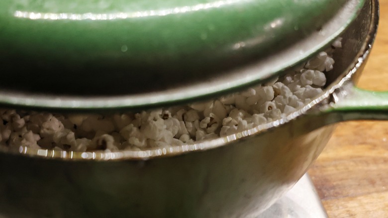 popping popcorn seen through crack below lid of green dutch oven