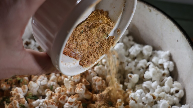 hand pouring a ramekin of seasoning mix into a pot of popcorn