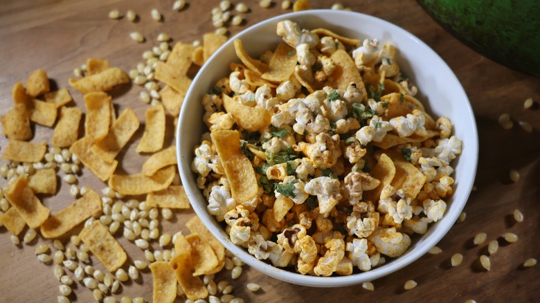 bowl of Frito pie popcorn on wooden table with Fritos chips and popcorn kernels surrounding it