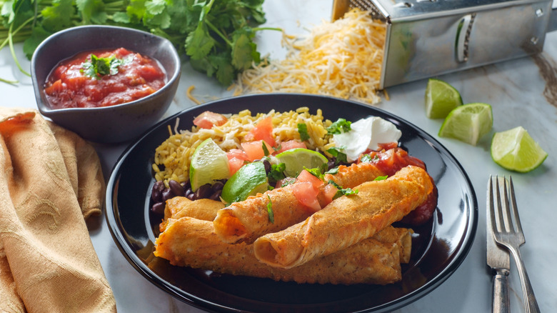 taquitos on plate with grated cheese and salsa