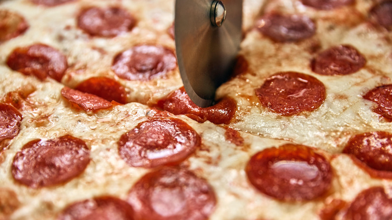 greasy pepperoni pizza being cut