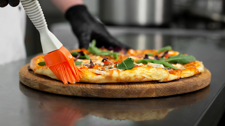 chef brushing olive oil on pizza crust