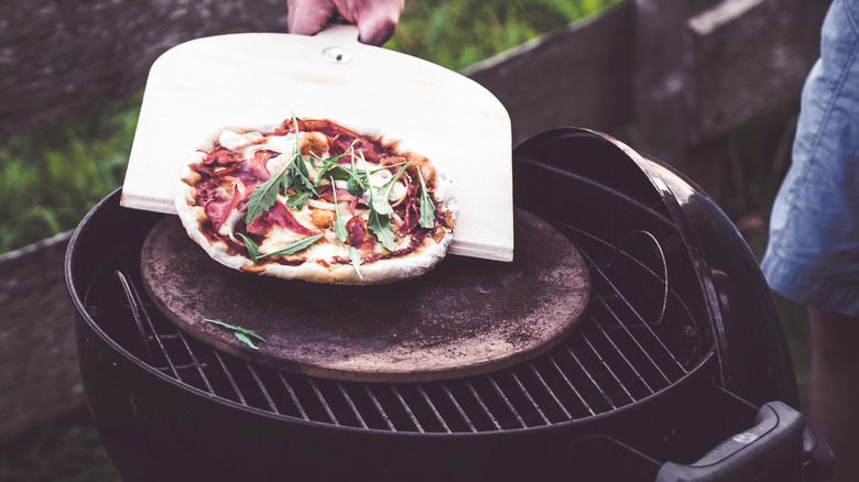 putting a pizza on the grill with a wooden peel