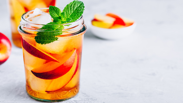 two peach summer drinks next to a small bowl of fresh peach wedges