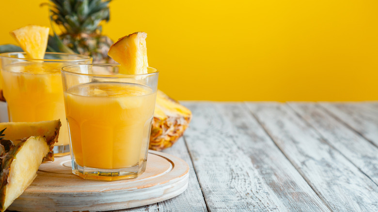 pineapple juice on a wooden board surrounded by fres pineapple and a yellow background