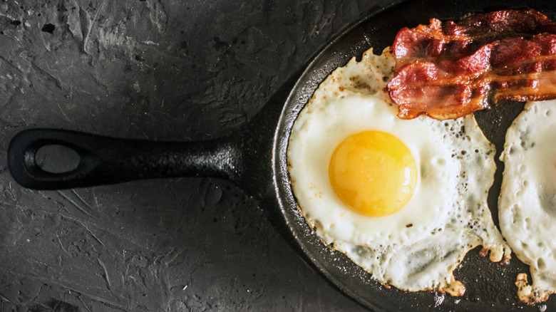 egg frying in cast iron skillet with bacon 