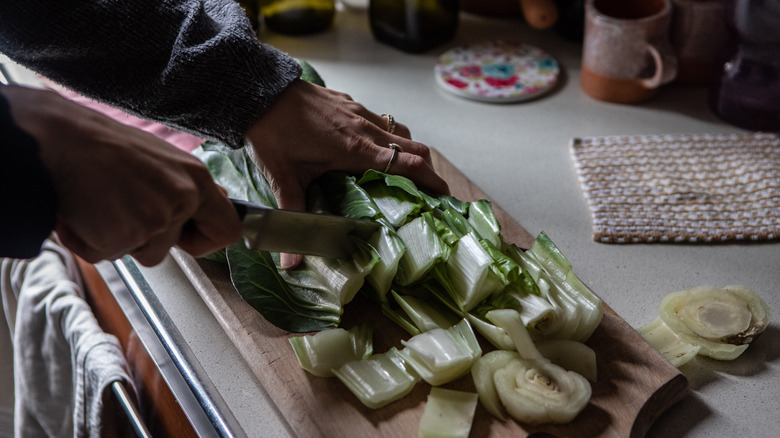 Person chopping green vegetable on wood