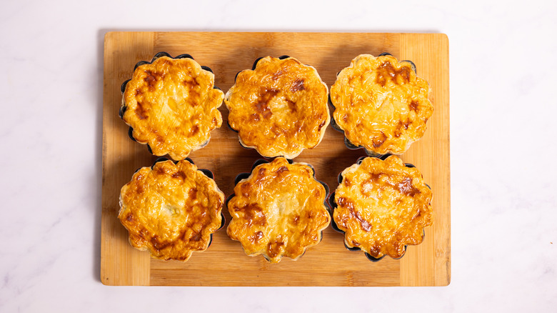 six golden pot pies on wooden board